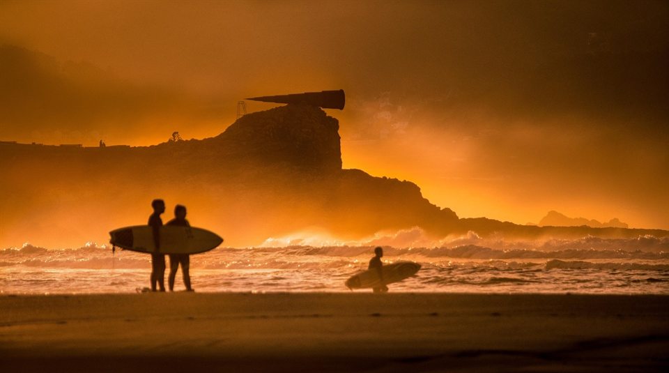 Surfers carrying their boards into the sea at sunset